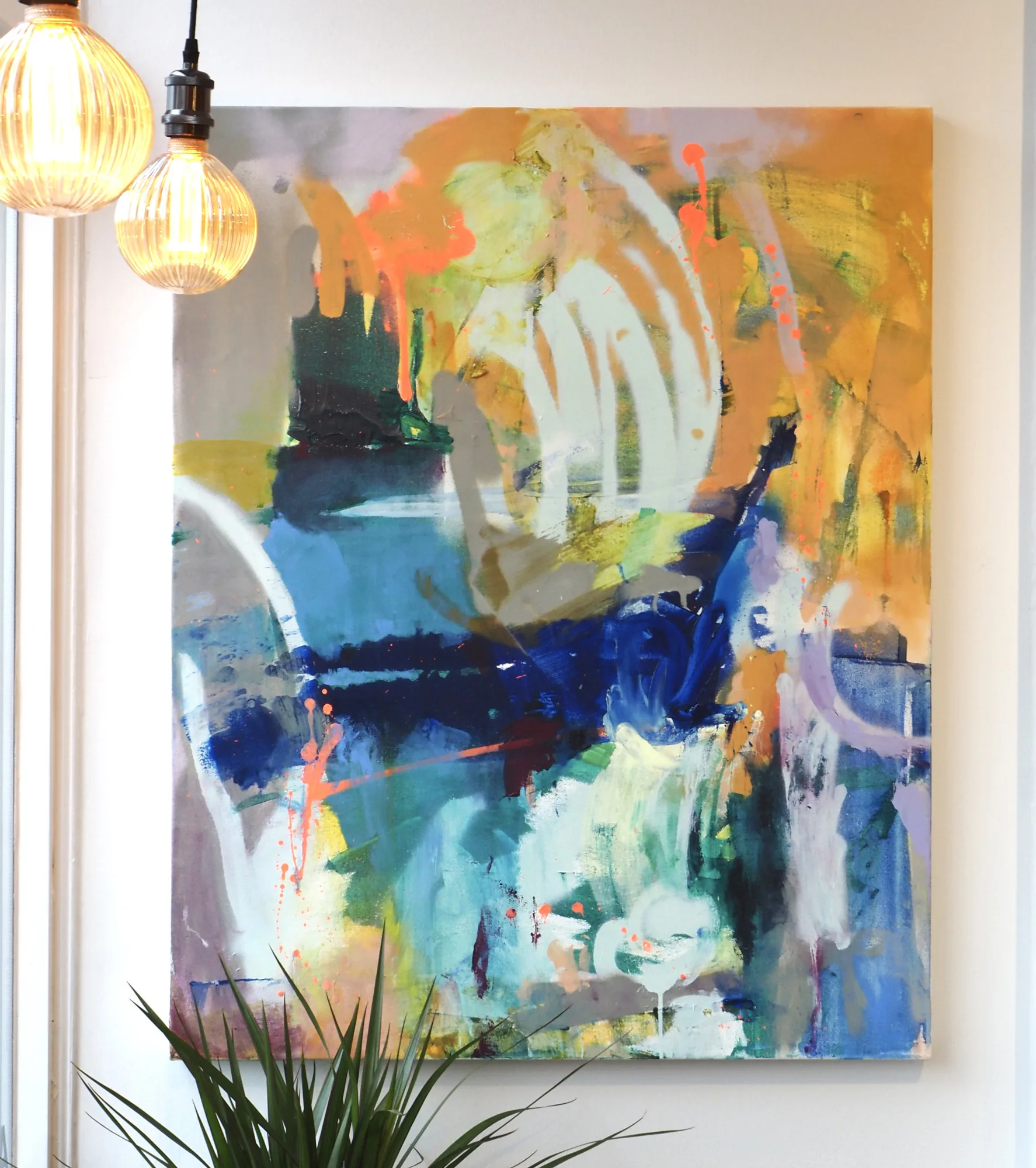 An abstract in blue, ochre and orange hung beside pendant lights